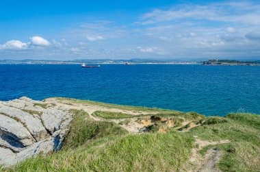 Santander 'in yeşil, kayalık kıyıları, Cantabria, Kuzey İspanya, arka planda tekneler