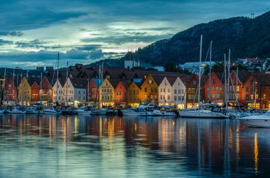 BERGEN, NORway - 16 Temmuz 2014: Vagen limanının arka planda Bryggen 'in renkli binaları ve Bergen, Norveç' te alacakaranlıkta görüntüsü. Bryggen, 1979 yılından beri UNESCO Dünya Kültür Mirası 'nda yer alıyor.