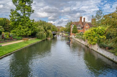 CAMBRIDGE, İngiltere - 11 Ekim 2014: Cambridge, İngiltere 'deki River Cam' de Pting. Tekne, küçük nehirlerde ve sığ sularda kullanılmak üzere tasarlanmış kare kesimli yayı olan düz tabanlı bir teknedir. Bahisçi vuruşu nehir yatağına doğru itiyor.