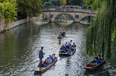 CAMBRIDGE, İngiltere - 11 Ekim 2014: Cambridge, İngiltere 'deki River Cam' de Pting. Tekne, küçük nehirlerde ve sığ sularda kullanılmak üzere tasarlanmış kare kesimli yayı olan düz tabanlı bir teknedir. Bahisçi vuruşu nehir yatağına doğru itiyor.
