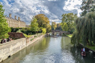 CAMBRIDGE, İngiltere - 11 Ekim 2014: Cambridge, İngiltere 'deki River Cam' de Pting. Tekne, küçük nehirlerde ve sığ sularda kullanılmak üzere tasarlanmış kare kesimli yayı olan düz tabanlı bir teknedir. Bahisçi vuruşu nehir yatağına doğru itiyor.