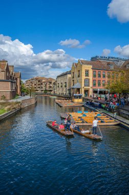 CAMBRIDGE, İngiltere - 11 Ekim 2014: Cambridge, İngiltere 'deki River Cam' de Pting. Tekne, küçük nehirlerde ve sığ sularda kullanılmak üzere tasarlanmış kare kesimli yayı olan düz tabanlı bir teknedir. Bahisçi vuruşu nehir yatağına doğru itiyor.