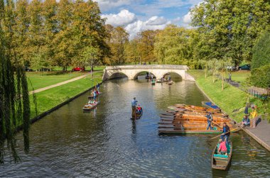 CAMBRIDGE, İngiltere - 11 Ekim 2014: Cambridge, İngiltere 'deki River Cam' de Pting. Tekne, küçük nehirlerde ve sığ sularda kullanılmak üzere tasarlanmış kare kesimli yayı olan düz tabanlı bir teknedir. Bahisçi vuruşu nehir yatağına doğru itiyor.