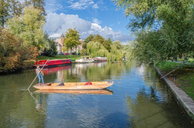 CAMBRIDGE, İngiltere - 11 Ekim 2014: Cambridge, İngiltere 'deki River Cam' de Pting. Tekne, küçük nehirlerde ve sığ sularda kullanılmak üzere tasarlanmış kare kesimli yayı olan düz tabanlı bir teknedir. Bahisçi vuruşu nehir yatağına doğru itiyor.