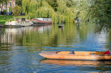 CAMBRIDGE, İngiltere - 11 Ekim 2014: Cambridge, İngiltere 'deki River Cam' de Pting. Tekne, küçük nehirlerde ve sığ sularda kullanılmak üzere tasarlanmış kare kesimli yayı olan düz tabanlı bir teknedir. Bahisçi vuruşu nehir yatağına doğru itiyor.