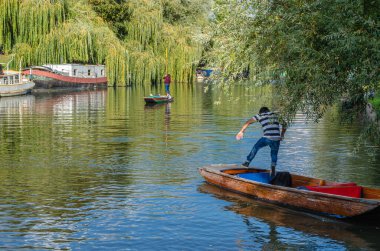 CAMBRIDGE, UK - OCTOBER 11, 2014: Punting on the River Cam in Cambridge, England. A punt is a flat-bottomed boat with a square-cut bow, designed for use in small rivers and shallow water. The punter propels the punt by pushing against the river bed w clipart