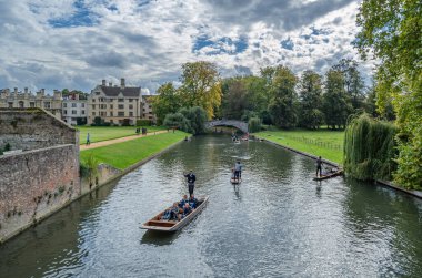 CAMBRIDGE, İngiltere - 11 Ekim 2014: Cambridge, İngiltere 'deki River Cam' de Pting. Tekne, küçük nehirlerde ve sığ sularda kullanılmak üzere tasarlanmış kare kesimli yayı olan düz tabanlı bir teknedir. Bahisçi vuruşu nehir yatağına doğru itiyor.