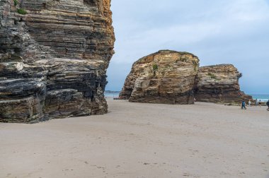 RIBADEO, İspanya - 30 AĞUSTOS 2022: Katedraller Plajı 'nı (Playa de las Catedrales) ziyaret eden insanlar, Galiçya' nın kuzeyindeki Ribadeo kentinde Doğal Anıt ilan ettiler. Adı uçurum oluşumlarından türetilmiştir. Karakter