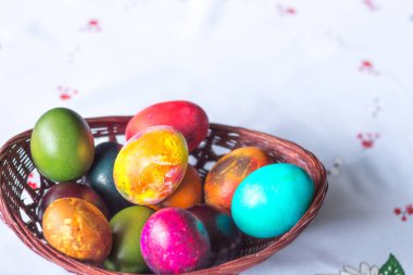 Beyaz masa örtüsü arkaplanındaki ahşap sepetteki renkli Paskalya yumurtalarının yükseltilmiş görüntüsü. Boşluğu kopyala.