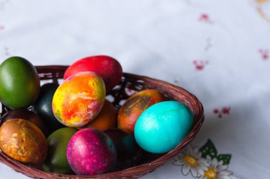 Beyaz masa örtüsü arkaplanındaki ahşap sepetteki renkli Paskalya yumurtalarının yükseltilmiş görüntüsü. Boşluğu kopyala.