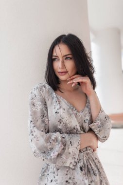 Güzel, taze yüzlü, şık, çiçekli yazlık elbiseli ve şehirde beyaz bir sütunun yanında poz veren güzel bir kız.