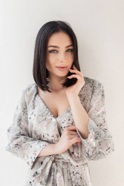 Çiçek desenli, şık, şık elbiseli güzel bir kadının yaz portresi. Açık havada beyaz bir duvarın yanında poz veriyor.