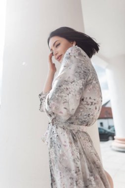 Şık, genç ve zarif bir kız. Şık bir saç stili ve şık bir klasik elbisesi var. Çiçek desenli, beyaz bir sütunun yanında güneşli bir günde şehirde yürüyor.