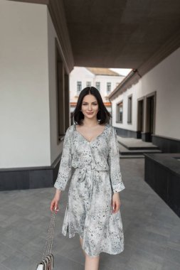 Şık, eski moda elbiseli, çiçekli ve şık çantalı güzel bir manken kız şehirde yürüyor.