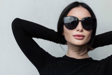 Şehirli moda kadın portresi. Seksi dudaklı, şık siyah gözlüklü. Gri arka planda siyah renkli gözlüklü.
