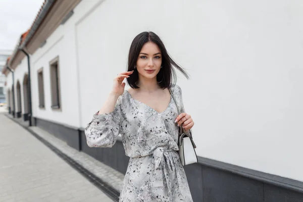 在城里散步的漂亮而优雅的女模特 留着蓬松的发型 穿着时髦的夏季花衣 提着一个包 — 图库照片