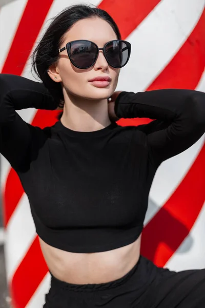 スタイリッシュなサングラスをかけた都会的なファッション美女性が赤い白い線の近くの通りの黒スポーツ衣装で — ストック写真