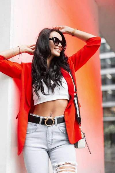 미소와 선글라스를 아름다운 여성붉은 재킷을 상의와 가방을 청바지를 비지니스 복장을 — 스톡 사진
