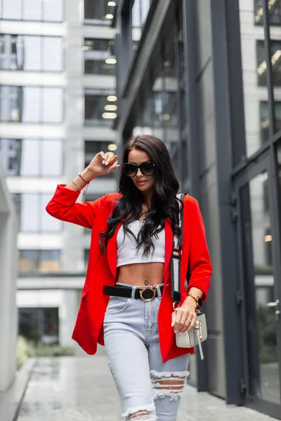 赤いブレザー ジーンズ 街を歩く財布とサングラスを身に着けている白いトップとファッショナブルな都会の衣装でスタイリッシュなカジュアルな女性 — ストック写真
