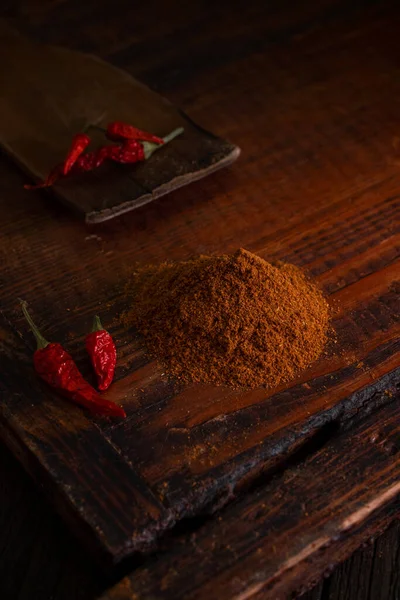 Spicy seasoning ground pepper and red dried chili peppers on a wooden board in a dark background, close-up