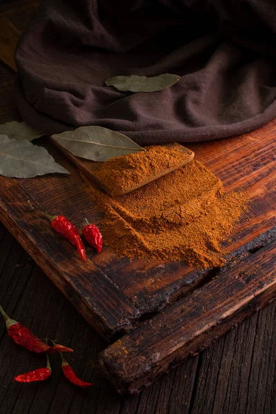 Spicy ground red spice with red dried chili peppers on a wooden brown table with leaves and a fabric