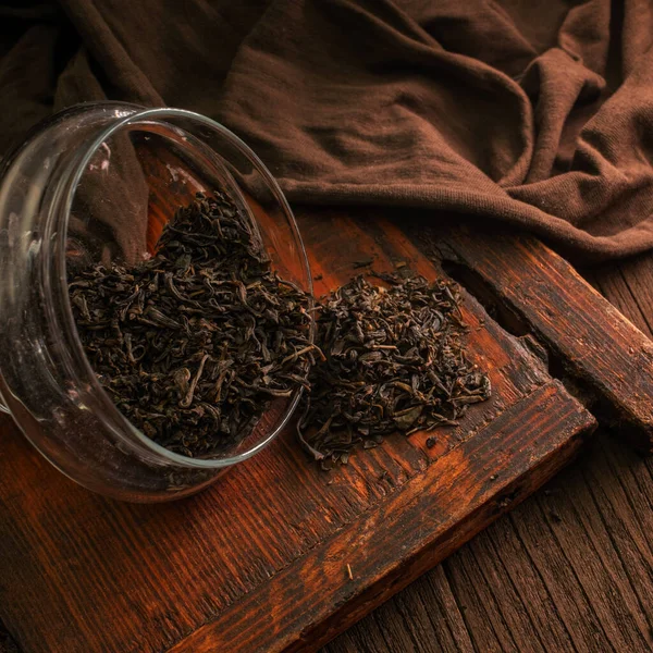 stock image Delicious dried green tea leaves in a glass jar on a wooden brown board on a dark background, closeup