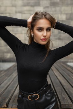 Glamorous urban stylish beautiful woman model in fashion trendy black clothes with gold chain and earring posing in the city