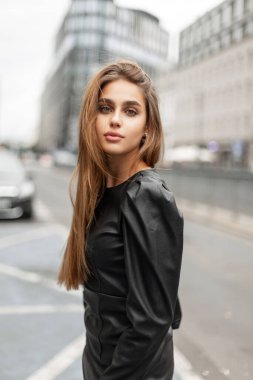 Pretty fashion woman in black leather dress walks in the modern city. Urban beauty girl
