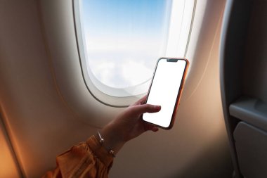 Girl is sitting on the plane and holding a mockup phone. Business, travel and work. Woman using smartphone