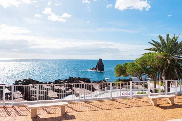 Beautiful view of the blue ocean with the sky on the promenade with benches and palm trees. Holidays on the island of Madeira. Atlantic Ocean