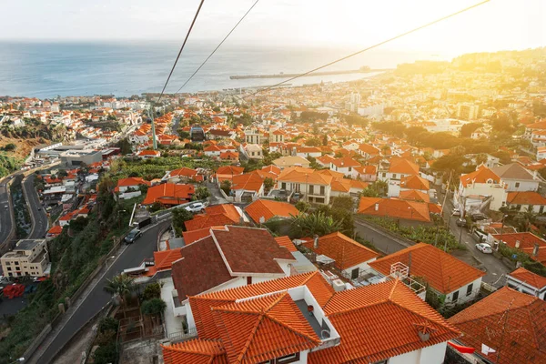 Amazing beautiful city of Funchal with orange roofs on the island of Madeira by the ocean at sunset, view from above. Ride on cable cars over the city from the mountain