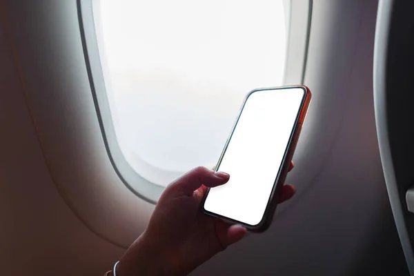 successful business woman is flying in an airplane and using a smartphone near the porthole. Mockup phone. Girl holding smartphone with white screen, free space for design