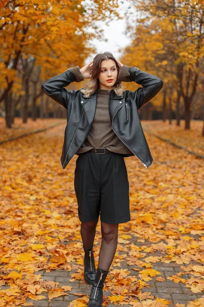 明るい黄色の葉を持つ秋の公園で革のジャケットとセーターの散歩でカジュアルな服のファッショナブルな若い女の子 — ストック写真