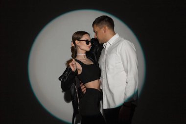 Şık, genç bir çift ve şık kıyafetler giyen, deri ceketli, beyaz gömlekli, güneş gözlüklü, yaratıcı, yuvarlak ışıklı bir stüdyoda.