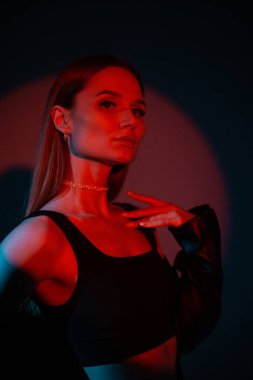 Yaratıcı, koyu renkli, siyah arka planda kırmızı ışıkları olan moda elbiseli güzel bir kadının stüdyo resmi.