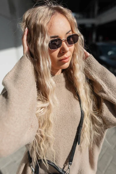 아름다운 금발의 금발의 아름다운 소녀가 유행하는 베이지 스웨터를 가방을 시내를 — 스톡 사진