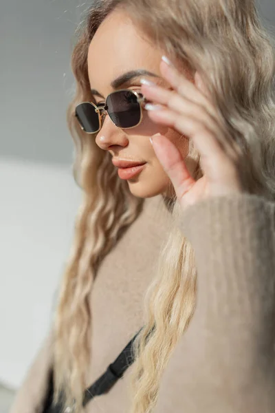 금발에 곱슬머리의 금발의 아름다운 소녀가 유행하는 베이지 스웨터를 빈티지 선글라스를 — 스톡 사진