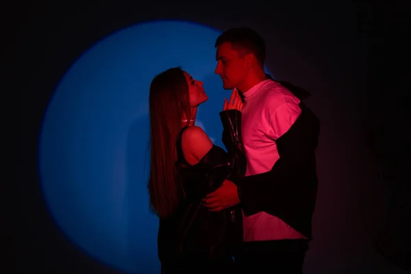 Stylish beautiful young couple man and pretty woman in fashionable clothes with red light on dark blue background in studio