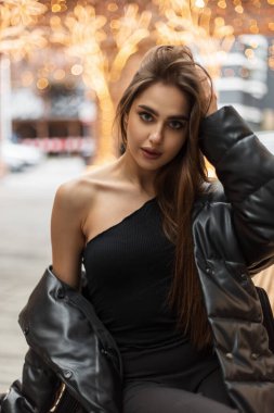 Moda mankeni, tek omuzlu, seksi bir manken, şehirde bir bankta oturuyor ve saçını düzeltiyor.