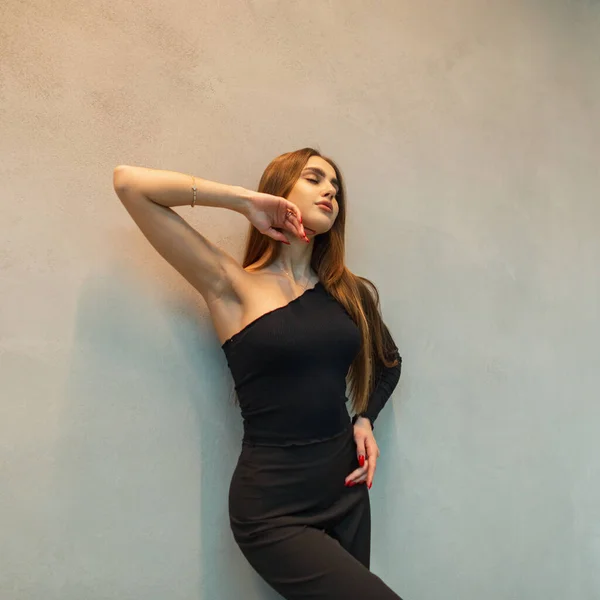 漂亮优雅的年轻姑娘 穿着时髦的黑色衣服 头戴单肩上衣 站在灰色的墙边 — 图库照片