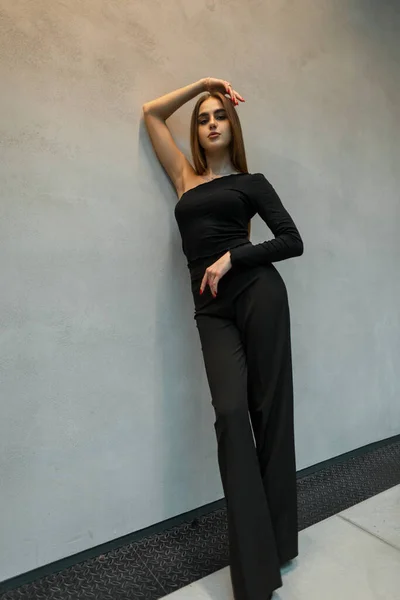 穿着时髦黑色衣服的时髦纤细而优雅的女人站在灰色的墙边 — 图库照片
