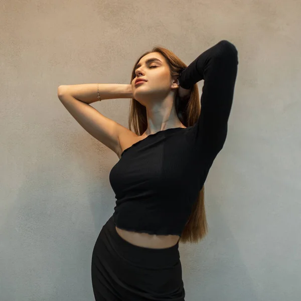 穿着时尚的黑色衣服 头戴高顶的造型 在灰色的墙壁边享受着时尚而美丽 优雅的女孩 — 图库照片