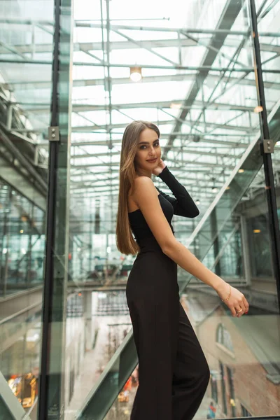时尚时尚漂亮的女经理穿着时髦的黑色典雅服装 头戴裤子 走在玻璃现代建筑中 她是一位美丽而快乐的女经理 — 图库照片