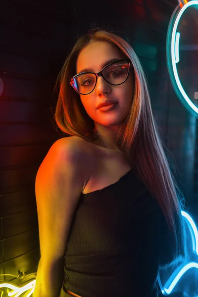 Siyah Giysili Gözlüklü Şık Genç Bir Kadın Renkli Neon Işıkları — Stok fotoğraf