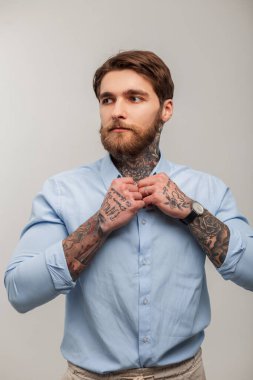 Havalı, başarılı, yakışıklı, dövmeli, sakallı, mavi tişörtlü, beyaz arka planda düğmesi olan hippi bir iş adamı. Erkek stüdyo portresi