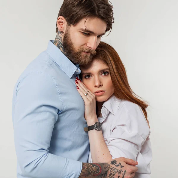 Beautiful fashion couple pretty redheaded girl and stylish brutal man in a blue shirt hug on a white background