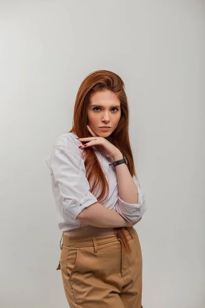 Elegant beautiful redhead woman in casual fashion outfit with white shirt and pants in a white background