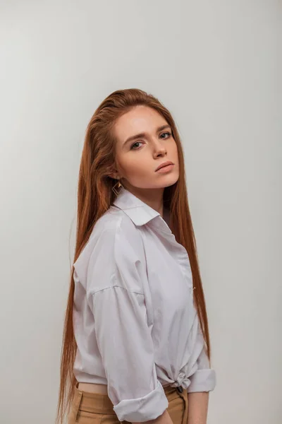 Fashion elegant female portrait of beautiful redhead fresh woman model in stylish white shirt stands on a white background. Beauty girl