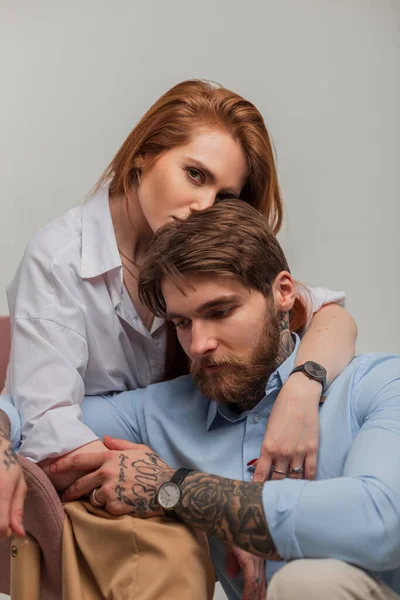 stock image Fashionable beautiful stylish couple in trendy elegant clothes in the studio. Handsome brutal man with beard and tattoo and beautiful redhead fashion woman