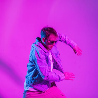Moda kıyafetleri içinde şık, genç hip hop dansçısı yaratıcı pembe ve mavi ışıklı stüdyoda dans ediyor.
